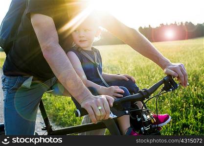 Father and baby daughter riding bike together, mid section