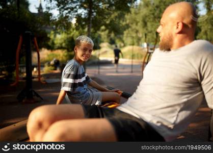 Father and boy doing abs exercise, sport training on playground outdoors. The family leads a healthy lifestyle, fitness workout in summer park. Father and boy doing abs exercise on playground
