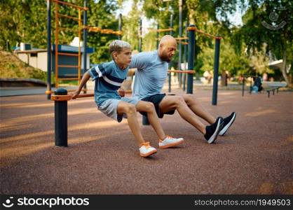 Father and boy doing exercise, sport training on playground outdoors. The family leads a healthy lifestyle, fitness workout in summer park. Father and boy doing exercise, sport training