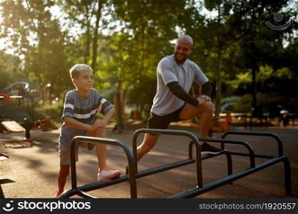 Father and boy doing stretching exercise, sport training on playground outdoors. The family leads a healthy lifestyle, fitness workout in summer park. Father and boy, stretching exercise on playground