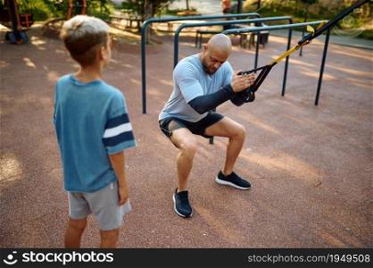 Father and boy, exercise with ropes, sport training on playground outdoors. The family leads a healthy lifestyle, fitness workout in summer park. Father and boy, exercise with ropes on playground