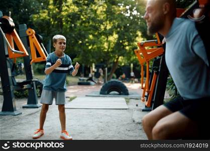 Father and boy on exercise machine, sport training on playground outdoors. The family leads a healthy lifestyle, fitness workout in summer park. Father and boy on exercise machine, sport training