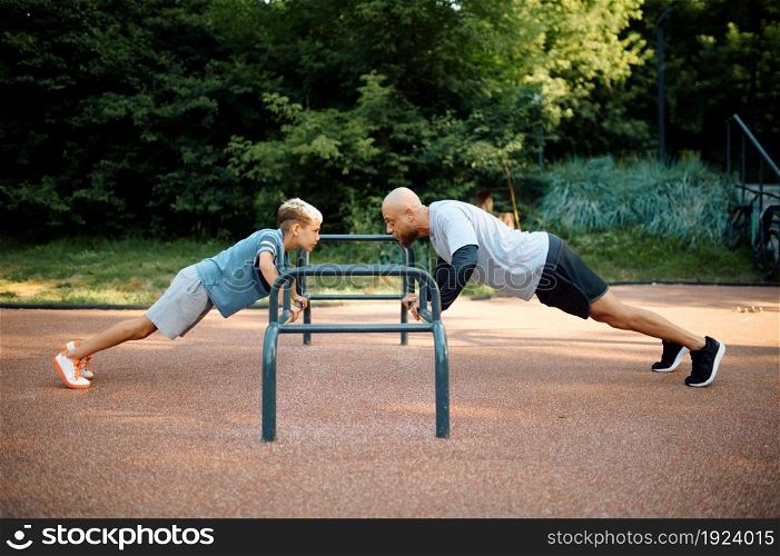 Father and boy, push-up exercise, sport training on playground outdoors. The family leads a healthy lifestyle, fitness workout in summer park. Father and boy, push-up exercise on playground