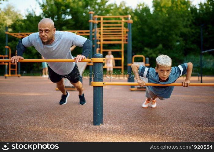 Father and child doing exercise, sport training on playground outdoors. The family leads a healthy lifestyle, fitness workout in summer park. Father and child doing exercise, sport training