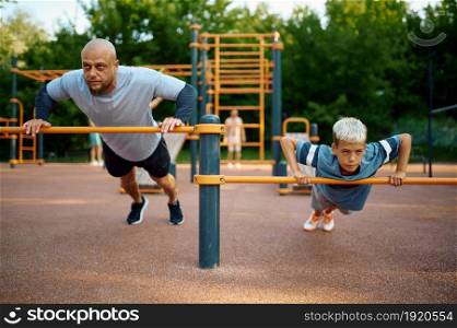 Father and child doing exercise, sport training on playground outdoors. The family leads a healthy lifestyle, fitness workout in summer park. Father and child doing exercise, sport training