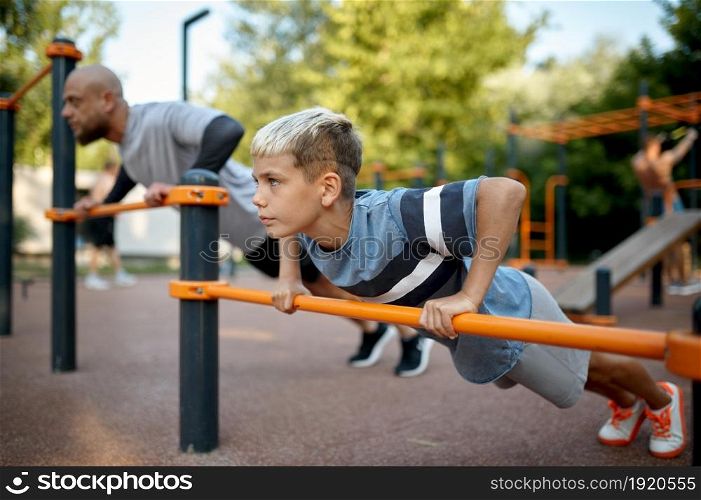 Father and child doing exercise, sport training on playground outdoors. The family leads a healthy lifestyle, fitness workout in summer park. Father and child doing exercise, sport training