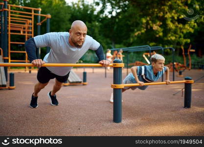 Father and child doing exercise, sport training on playground outdoors. The family leads a healthy lifestyle, fitness workout in summer park. Father and child doing exercise, sport training