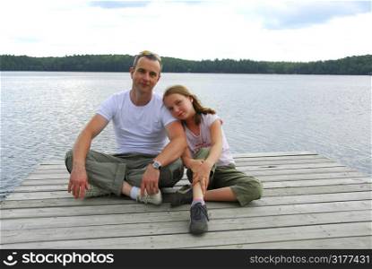 Father and child sitting on a wooden pier on a lake in nothern Ontrario