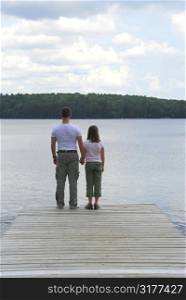 Father and child standing on a wooden pier on a lake holding hands