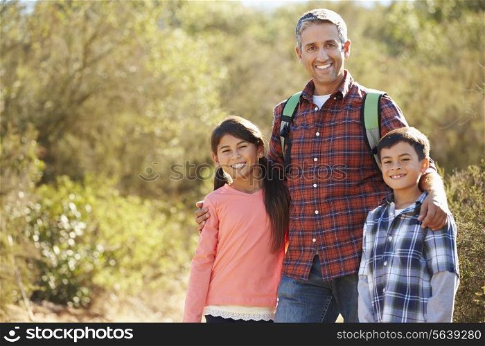 Father And Children Hiking In Countryside Wearing Backpacks