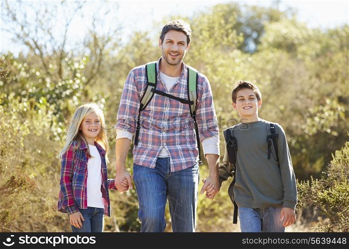 Father And Children Hiking In Countryside Wearing Backpacks