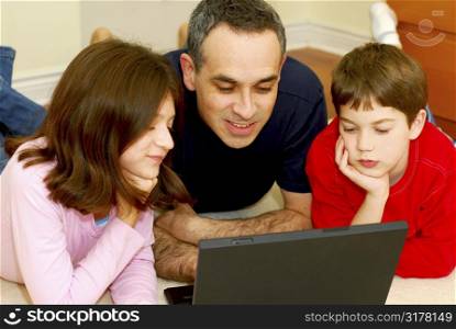 Father and children lying on the floor at home and looking into a portable computer
