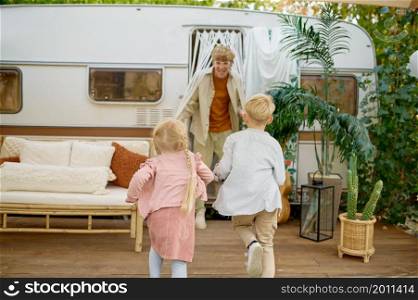 Father and children play at the trailer, summer camping. Family with kids travel in camp car, nature and forest on background. Campsite adventure, travelling lifestyle. Father and children play at the trailer, camping