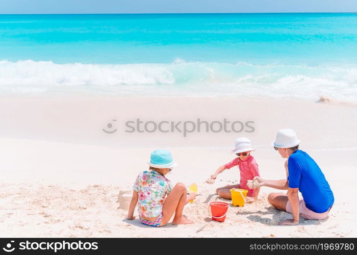 Father and children playing with sand on tropical beach. Father and kids making sand castle at tropical beach. Family playing with beach toys