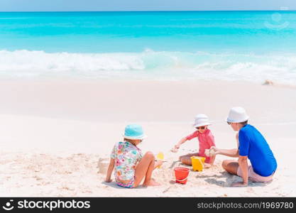 Father and children playing with sand on tropical beach. Father and kids making sand castle at tropical beach. Family playing with beach toys