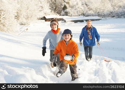 Father And Children Pulling Sledge Up Snowy Hill