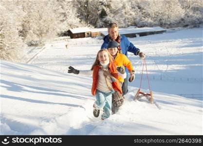 Father And Children Pulling Sledge Up Snowy Hill