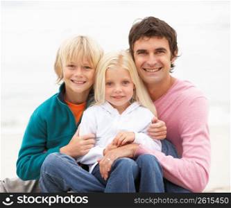 Father And Children Sitting On Winter Beach Together