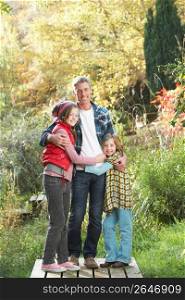 Father And Children Standing Outdoors On Wooden Walkway In Autumn Landscape