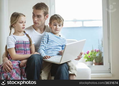 Father and children using laptop while sitting on chair