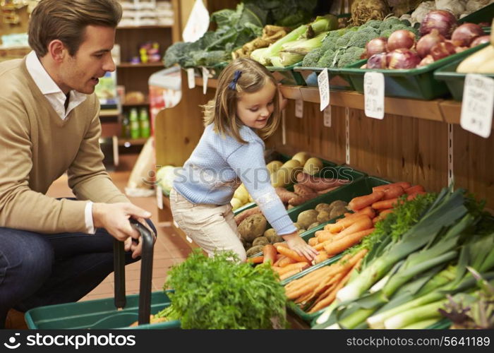 Father And Daughter Choosing Fresh Vegetables In Farm Shop