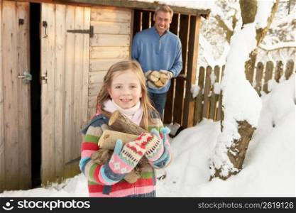 Father And Daughter Collecting Logs From Wooden Store In Snow