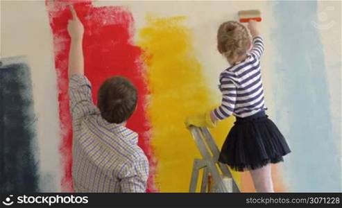 Father and daughter doing funny repair. They painting wall in different colors. Girl standing on the ladder and painting dads nose