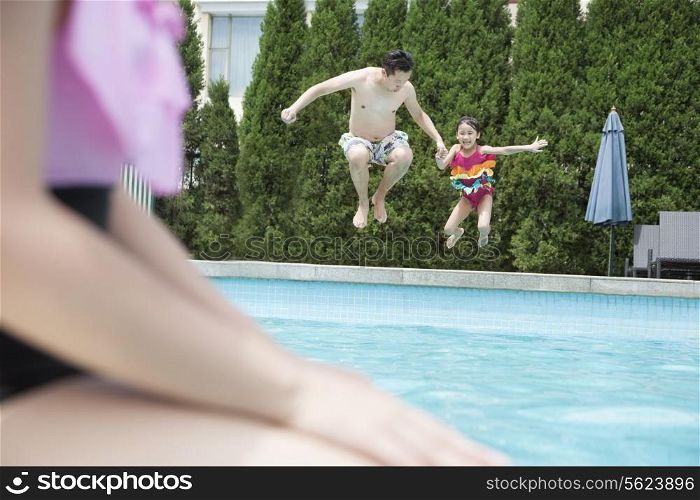 Father and daughter holding hands and jumping into the pool