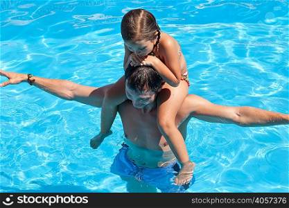 Father and daughter in outdoor pool, daughter sitting on father&acute;s shoulders, elevated view