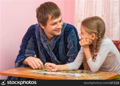 Father and daughter looked at each other collecting puzzle elements