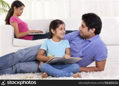 Father and daughter looking at each other while mother using laptop in the background