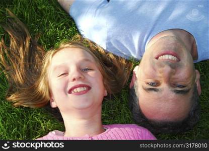 Father and daughter lying on green grass and looking up