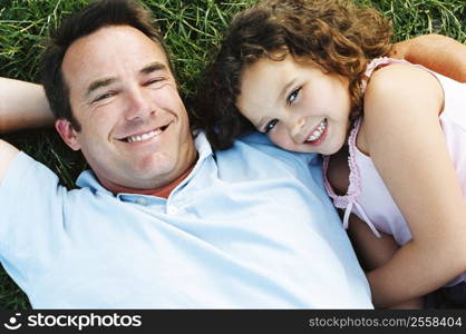 Father and daughter lying outdoors smiling