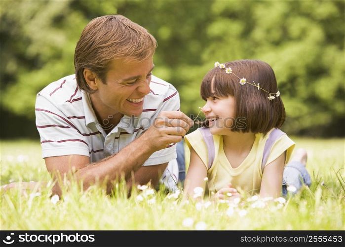 Father and daughter lying outdoors with flowers smiling