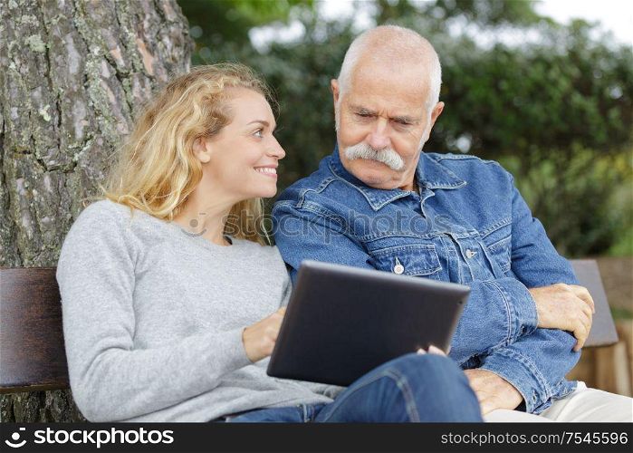 father and daughter on park bench looking at a tablet