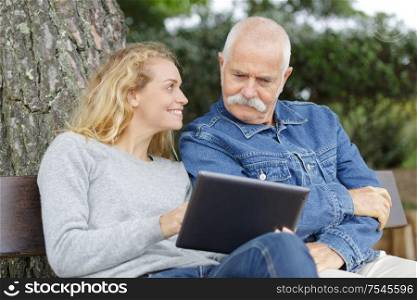 father and daughter on park bench looking at a tablet