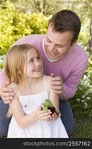 Father and daughter outdoors holding plant smiling