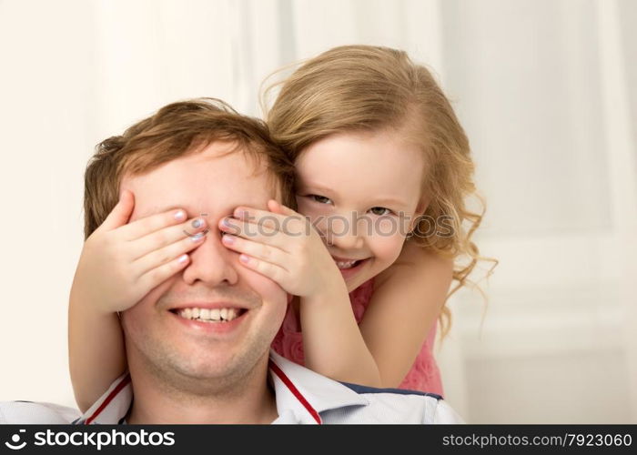 Father and daughter playing at home. Little girl closing dads eyes with hands and laughing. Family fun together. Daughter playing with father closing his eyes