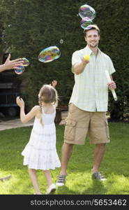 Father And Daughter Playing With Bubbles In Garden