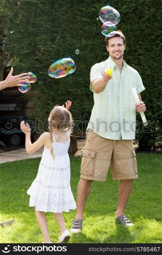 Father And Daughter Playing With Bubbles In Garden