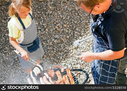 Father and daughter preparing meat and sausages using a barbecue grill