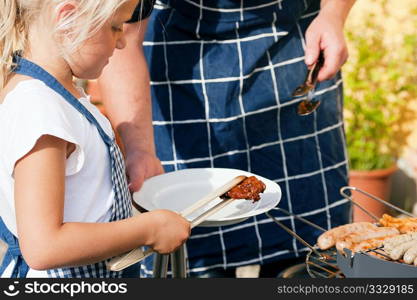 Father and daughter preparing meat and sausages using a barbecue grill
