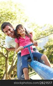 Father And Daughter Riding On See Saw In Playground