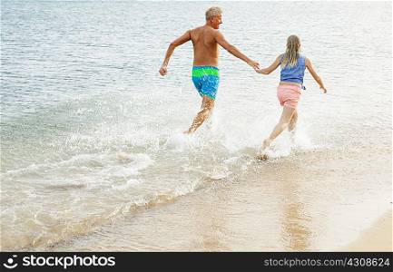 Father and daughter running and holding hands on beach