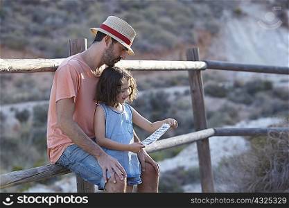 Father and daughter sitting on fence reading note, Almeria, Andalusia, Spain
