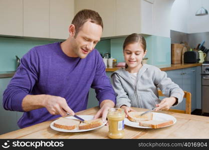 Father and daughter spreading peanut butter on bread