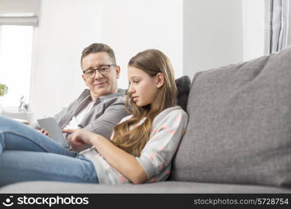 Father and daughter using digital tablet on sofa at home
