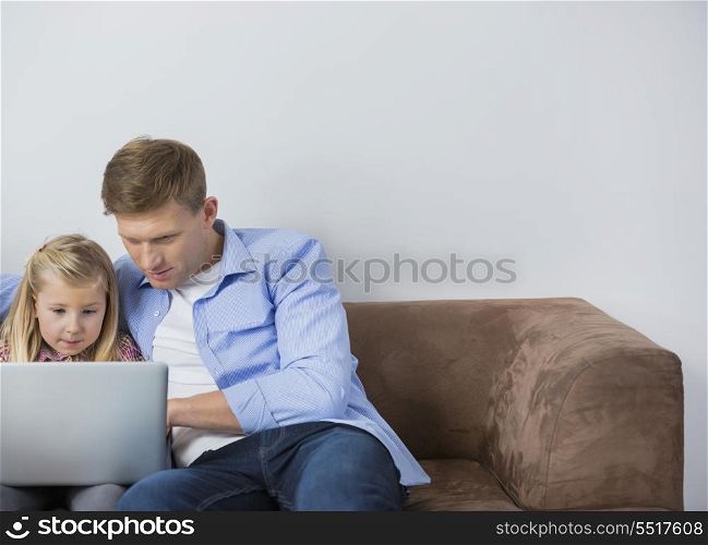 Father and daughter using laptop together on sofa at home