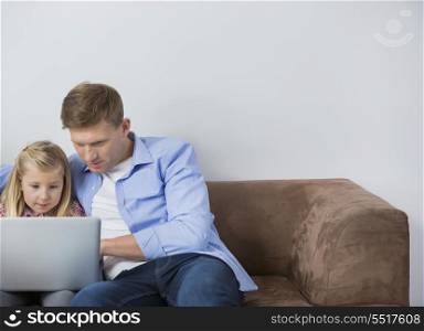 Father and daughter using laptop together on sofa at home