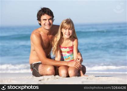 Father And Daughter Wearing Swimwear Sitting On Sandy Beach